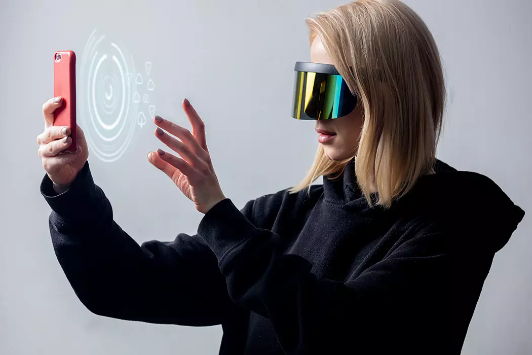 Mulher loira com celular e óculos IA representando a era phygital, que une os negócios físicos e digitais.